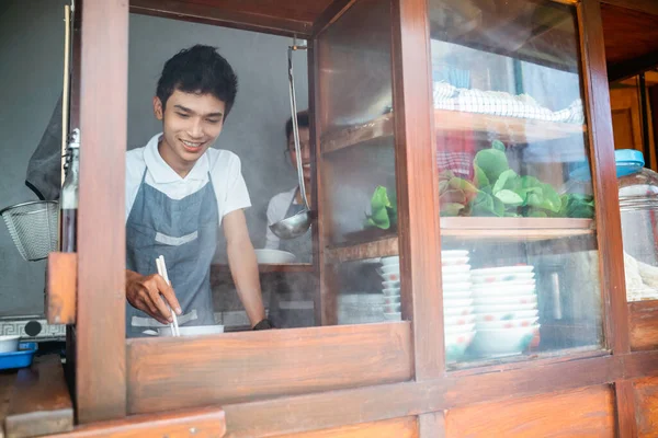 Asian salesman holding chopsticks while boiling noodles while selling using a cart