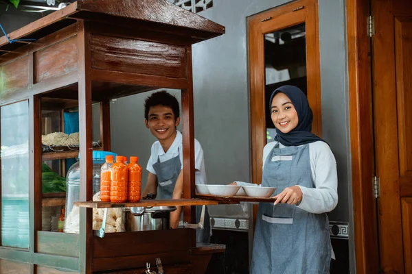 smiling two sellers preparing chicken noodles dish with bowls for customer