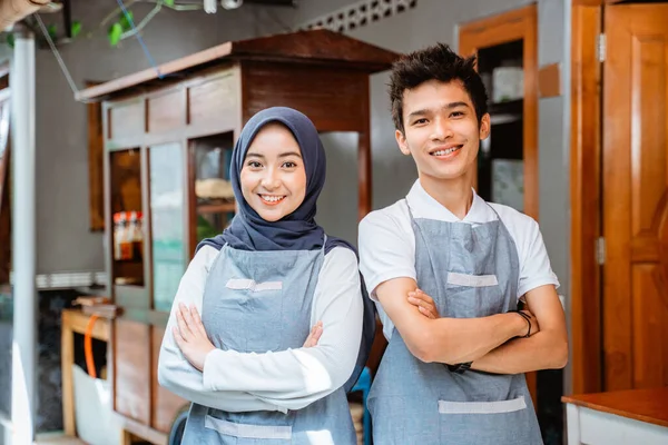 woman in headscarf and young man in apron with arms crossed smiling against chicken noodle cart background