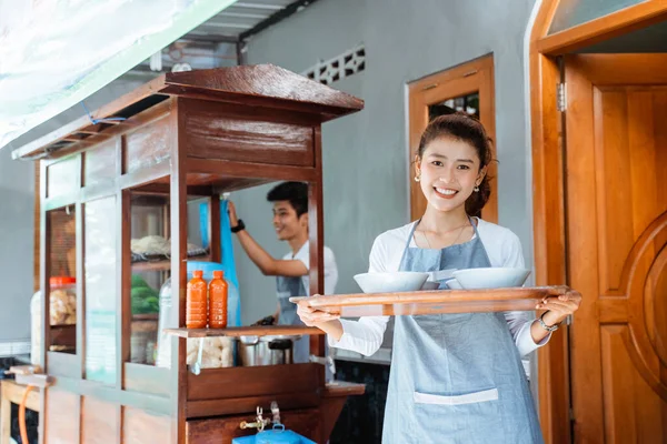 smiling woman carrying bowl of chicken noodles with tray on cart background