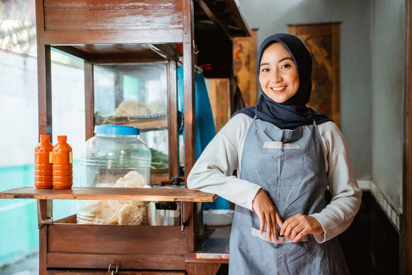 relaxed hijab woman wearing apron smiling while standing next to cart
