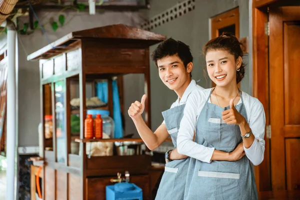 female and male traders smiling with thumbs up at a chicken noodle cart stall