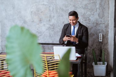 portrait of smiling businessman using smartphone while sitting in cafe by himself