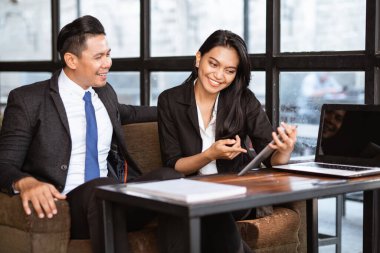 happy asian businessman and woman having a relaxed meeting using tablet in cafe