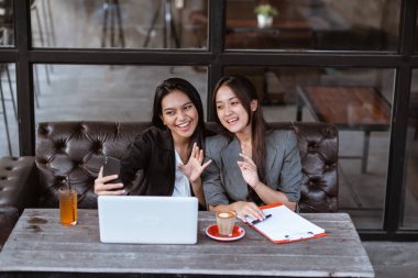 two attractive asian female worker make a video call conference using smartphone while sitting on a cafe