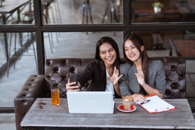 two attractive asian female worker make a video call conference using smartphone while sitting on a cafe
