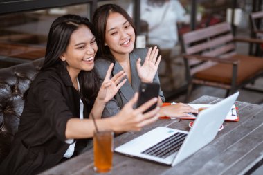 two attractive asian female worker make a video call conference using smartphone while sitting on a cafe