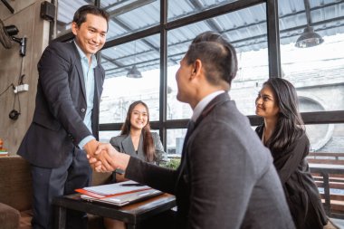happy two young business partner and executive shaking hands in the cafe