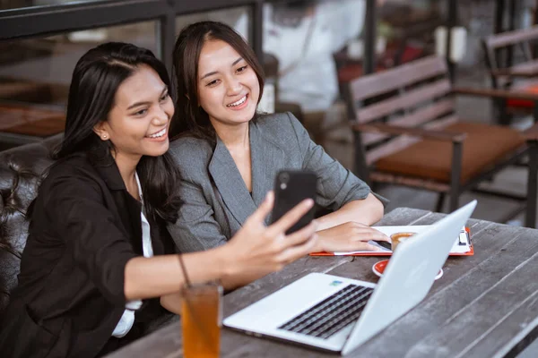 two attractive asian female worker make a video call conference using smartphone while sitting on a cafe
