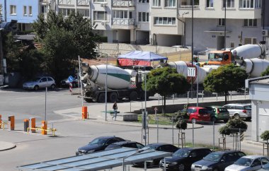 Şehirdeki bir inşaat sahasının yakınında ağır beton kamyonlar bekliyor. Kamyonlar ağır hava kirliliği yaratıyor.