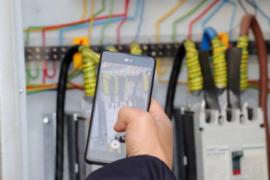 Kilowatt 'lık elektrik sayacını okuyan teknisyen akıllı telefon, gece gündüz kilovatlık gümrük tarifeleri kullanıyor.