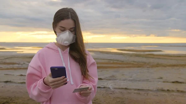 Maskeli genç bir kız gün batımında plajda kredi kartı bilgilerine giriyor. Yüksek kalite 4k görüntü