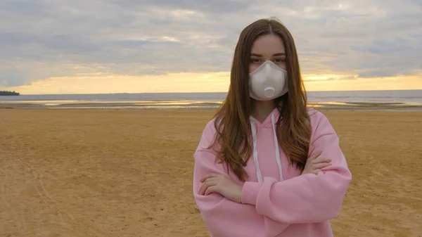 Maskeli üzgün bir kız kasvetli bir sahilde duruyor. Koronavirüs sırasında depresyon. Yüksek kalite 4k görüntü