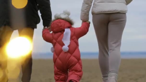 Anya és apa megtanítják járni a babát. Család séta a strandon — Stock videók