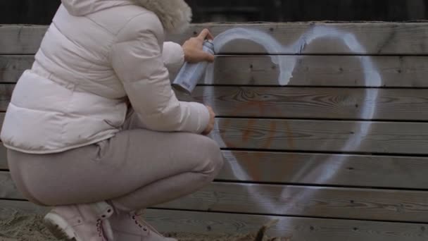 Egy sárga kalapos fiatal lány szívjelet rajzol a falra. A szeretet kinyilvánítása — Stock videók