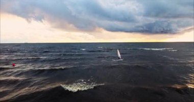 Rüzgar sörfçüsü batan güneşin altında fırtınada dalgalarda sörf yapar.