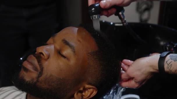 Парикмахер моет волосы и кожу клиенту, лежащему головой вперед в душевой раковине — стоковое видео