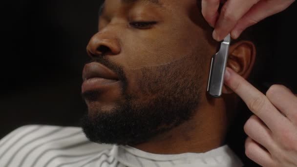 Muž holení vousy afrického Američana muže s rovnou břitvou v holičství — Stock video