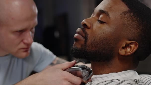 Белый парень бреет бороду триммером для афроамериканца - крупным планом — стоковое видео