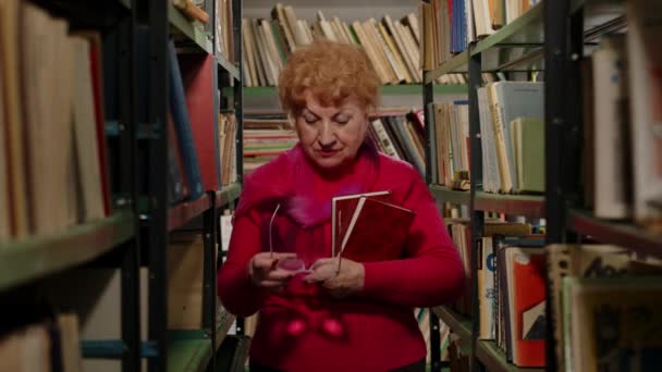 안경을 끼고 도서관에서 책을 들고 있는 똑똑 한 노인 선생님 — 비디오