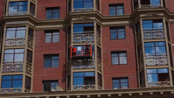 Будівельник виконує екстремальні роботи на висоті за межами будівлі. Інженер прив'язаний до робочої платформи — стокове відео