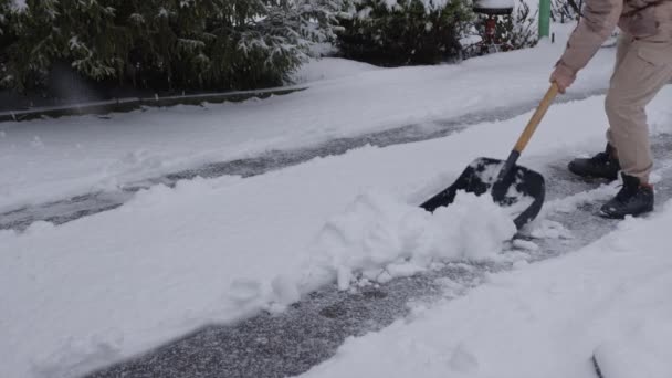 En ung fyr i vinterdragt rydder sne fra udgangen af garagen efter et snefald – Stock-video