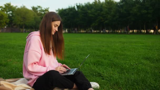 Seorang gadis muda yang cerdas melakukan tugas siswa di taman pada laptop. Belajar jarak — Stok Video