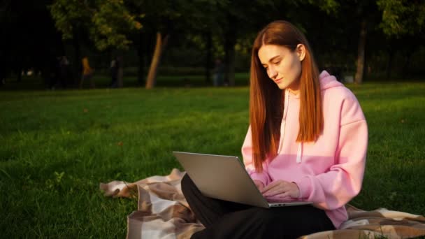 Gyönyörű fiatal lány diák dolgozik egy laptop egy parkban, közel az egyetemhez — Stock videók