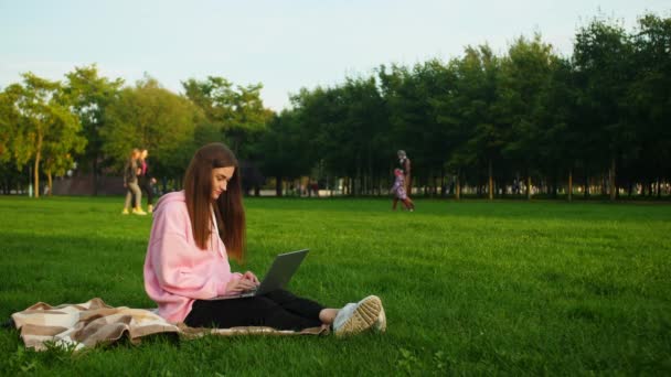 Seorang gadis muda yang cerdas melakukan tugas siswa di taman pada laptop. Belajar jarak — Stok Video