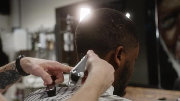 Profesjonalny fryzjer robi krótką fryzurę do młodego czarnego faceta - widok z tyłu — Wideo stockowe