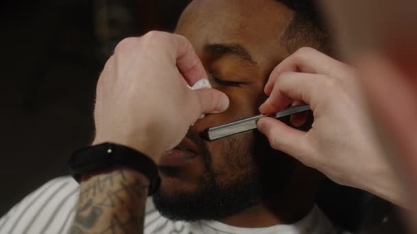 Afro-Amerikan bir adamın sakalını tıraş eden adam berber dükkanında ustura kullanıyor. — Stok video