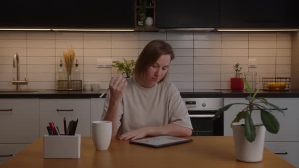 Pensativo designer europeu menina criativa trabalhando em casa na cozinha usando um tablet — Vídeo de Stock