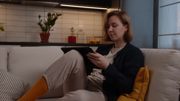 Artista chica natural se basa en una tableta digital mientras está sentado en un cómodo sofá en la sala de estar — Vídeos de Stock