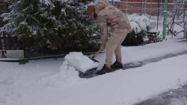 En ung fyr i vinterdragt rydder sne fra udgangen af garagen efter et snefald – Stock-video