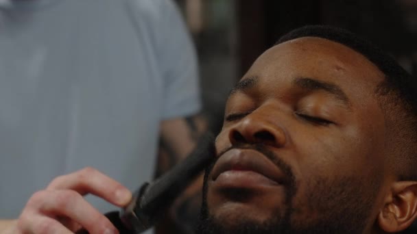 Парикмахер вытирает афроамериканцам лоб перед бритьем. Крупный план — стоковое видео