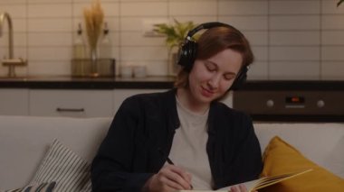 Gülümseyen kız öğrenci oturma odasında müzik dinler ve üniversitede sınavlara hazırlanır.