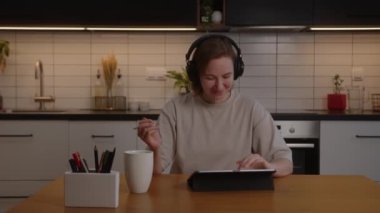 Kulaklıklı mutlu kız oturma odasında bir tablette çalışıyor ve müzik dinliyor.