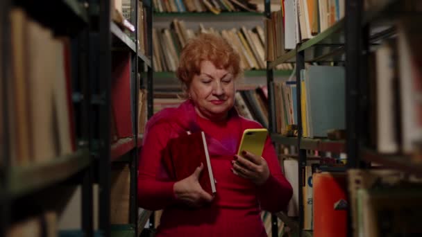 Una anciana toma una foto con libros en la biblioteca. Selfie para redes sociales — Vídeos de Stock