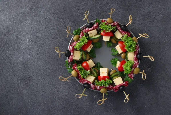 Canapele festive cu cârnați, castraveți, roșii, măsline și brânză, servite pe o farfurie ca coroană de Crăciun, pe un fundal gri închis — Fotografie, imagine de stoc