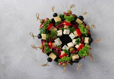 Sosisli, salatalıklı, domatesli, zeytinli ve peynirli şenlikli kanepeler, açık arkaplanlı bir Noel çelengi olarak bir tabakta servis ediliyor. Üst görünüm