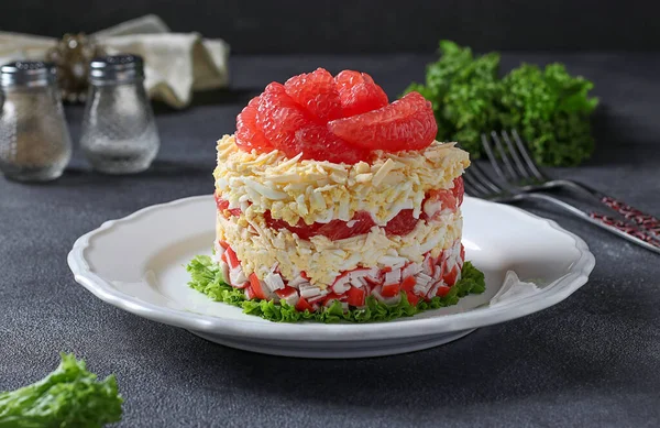 Праздничный салат с грейпфрутом, сыром и крабовыми палочками на белой тарелке на сером фоне — стоковое фото