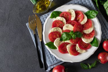 Dilimlenmiş domatesli Caprese salatası, mozzarella peyniri, fesleğen ve gri arka planda beyaz tabakta zeytinyağı, Top view