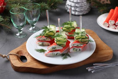 Yengeç çubuklu kanepeler, tahta tahtada beyaz tabakta peynir ve salatalık. Kutlama aperatifi