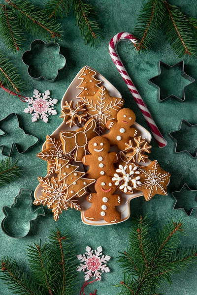 Homemade gingerbread cookies in a plate in the shape of christmas tree on green background. Xmas festive greeting card. Top view — Stock Photo, Image