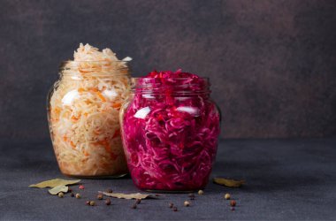Havuçlu ev yapımı lahana turşusu ve cam kavanozlarda pancar, koyu gri bir masa. Mayalanmış yiyecek. Boşluğu kopyala