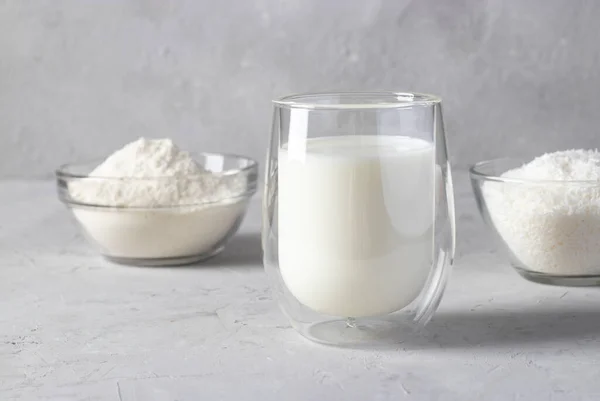 Prodotti a base di cocco: fiocchi di cocco, latte e farina in un piatto trasparente su fondo grigio chiaro. Note di alimentazione — Foto Stock