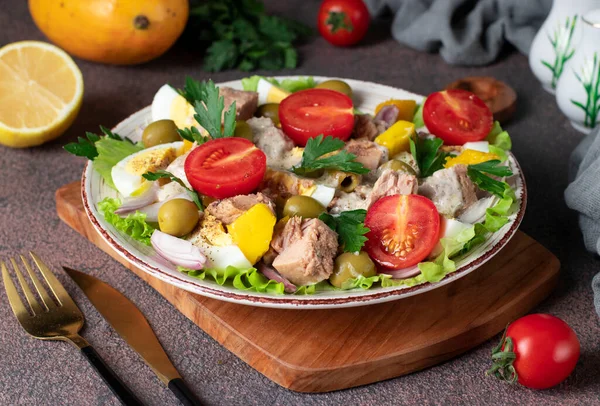 Salad with mango, tuna and cherry tomatoes served with green lettuce leaves in a plate on a brown background, Close-up — Stockfoto