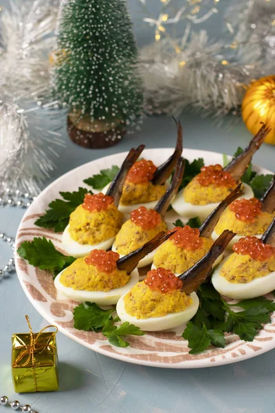 Вкусная праздничная закуска - Яйца фаршированные шпротами и красной икрой на тарелке на новогоднем голубом фоне — стоковое фото