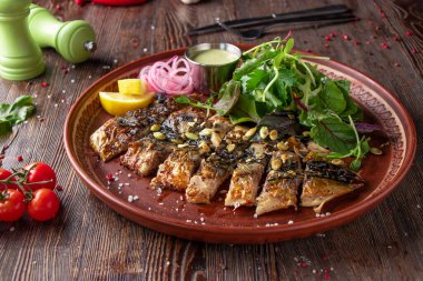 Ahşap masada soslu, soğanlı, limonlu ve yeşil salatalı ızgara uskumru.