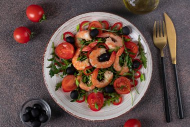 Karidesli salata, roka, vişneli domates ve kahverengi arka planda zeytinyağlı siyah zeytin.